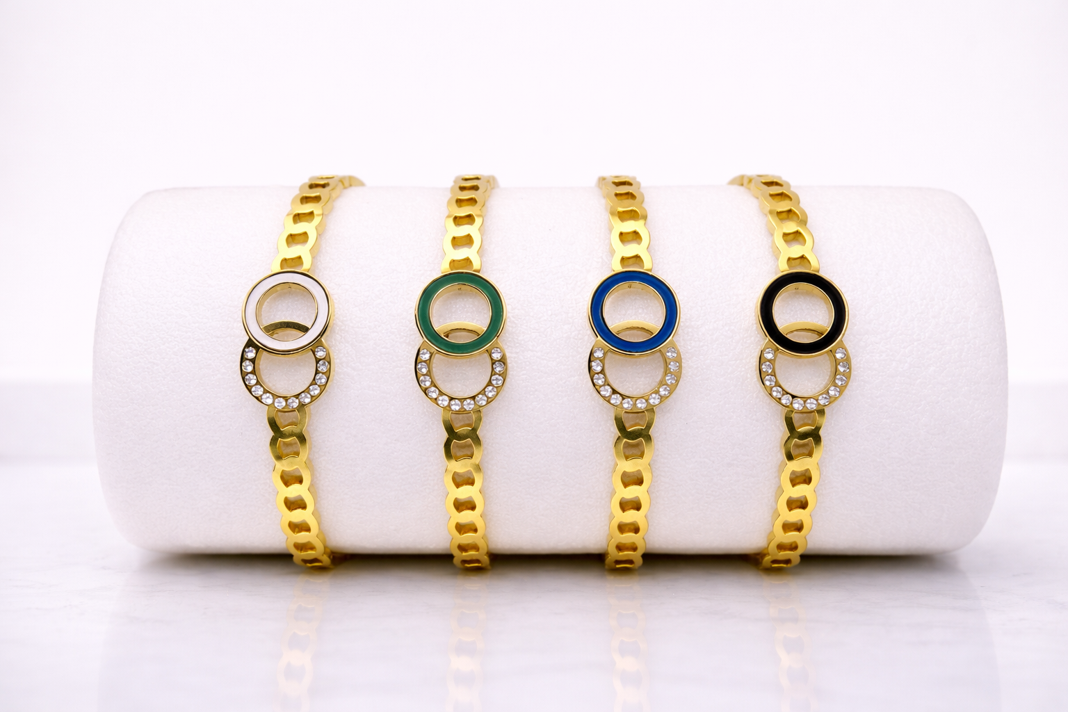 Four gold bracelets with colored centers on a white cylindrical stand.